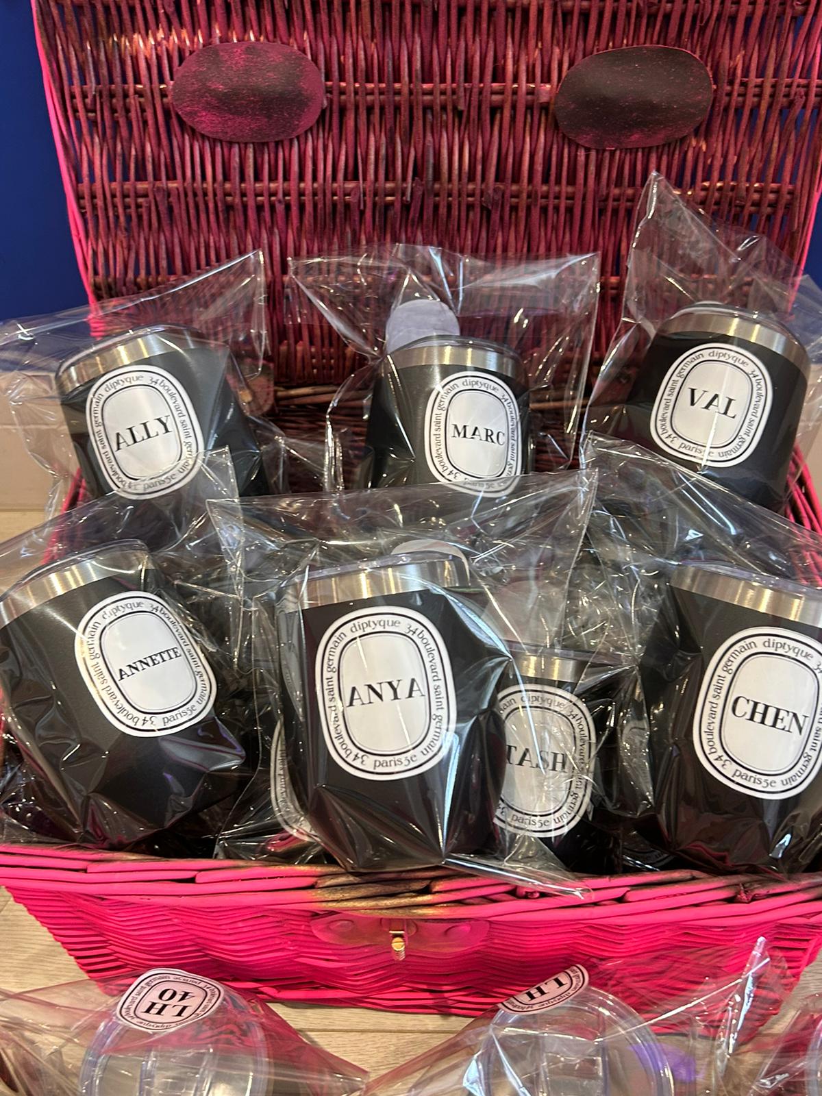 Assorted black travel cups with name labels in a pink basket