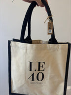 Beige personalised tote bag with 'LE 40 Tenerife 2025' text and black handles, held by a hand.
