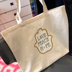 Beige tote bag with 'Love Peace Hope' text on a chair.