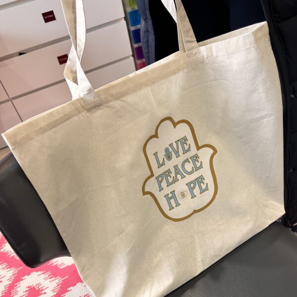 Beige tote bag with 'Love Peace Hope' text on a chair.