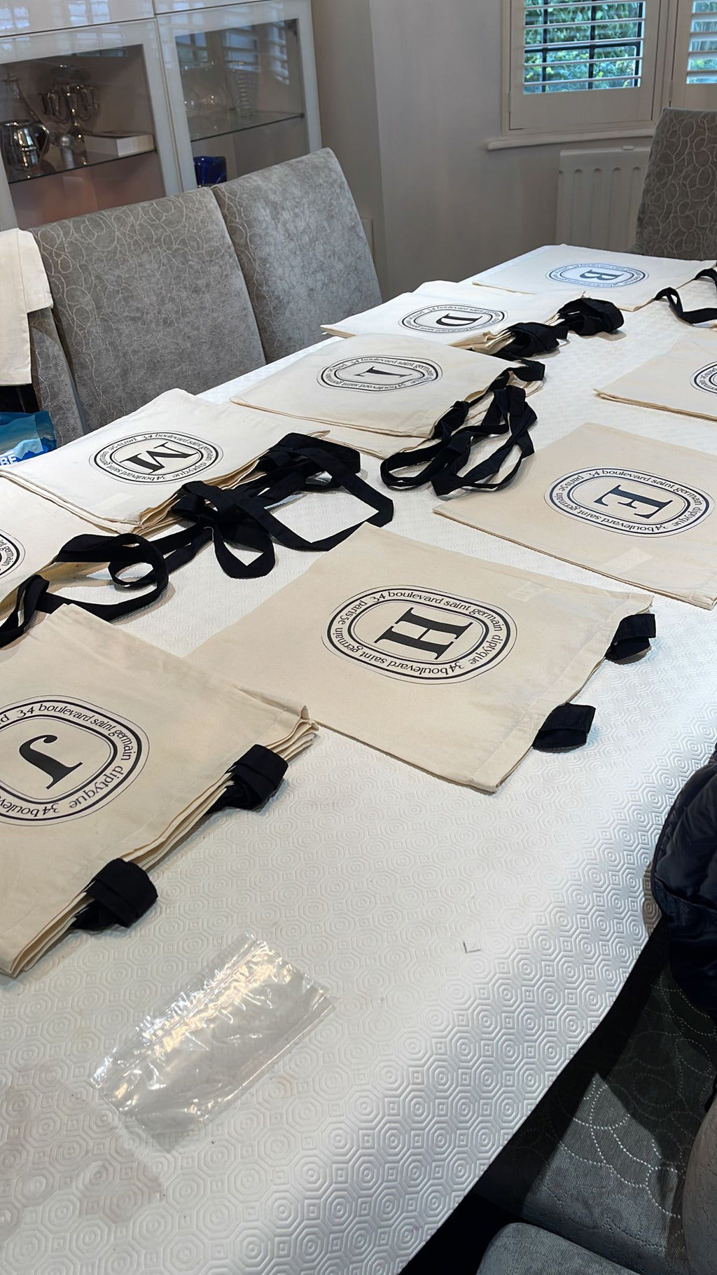 Beige tote bags with well-known brand look with a logo on a white table in a room with chairs and a window