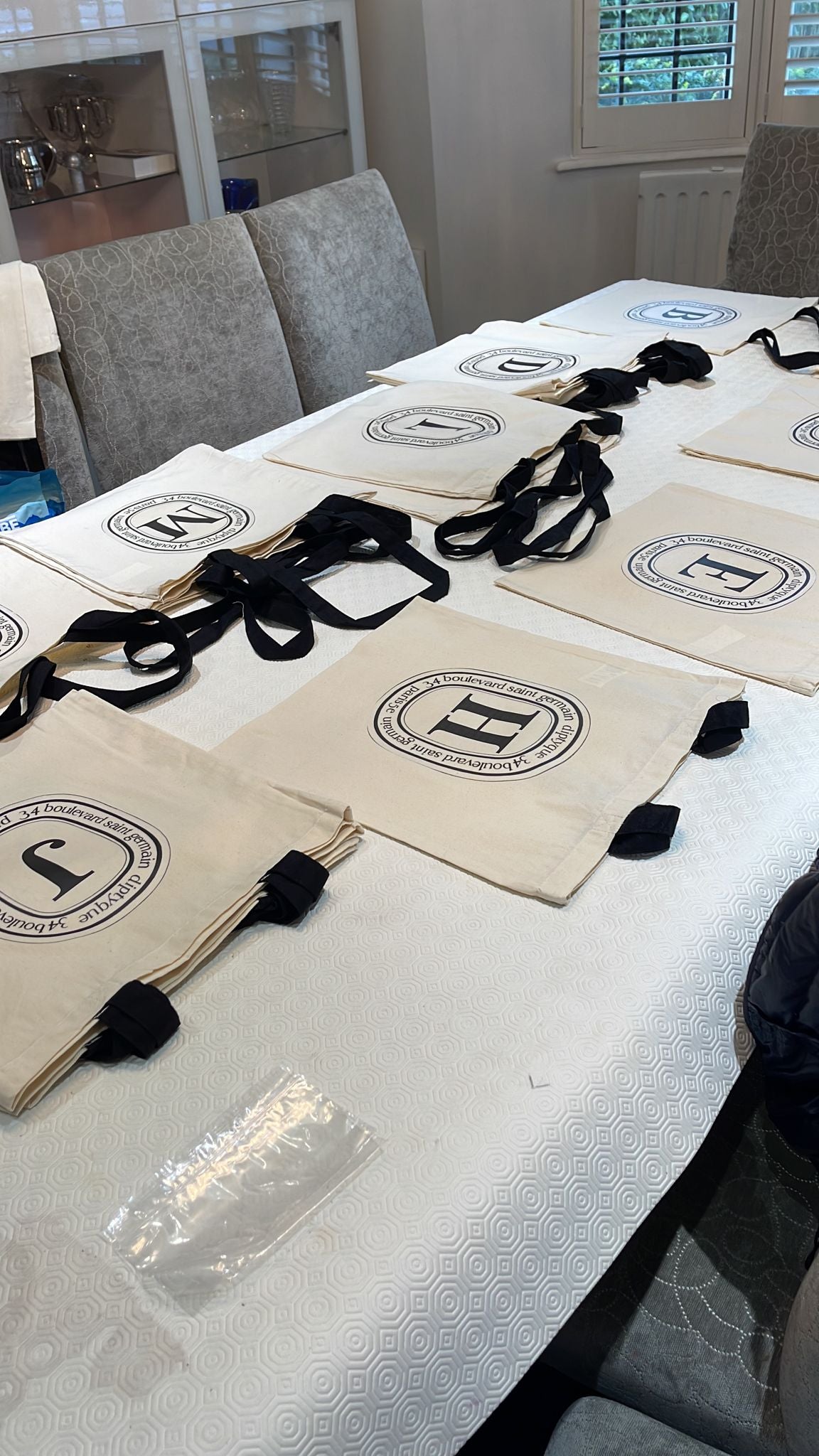 Beige tote bags with well-known brand look with a logo on a white table in a room with chairs and a window