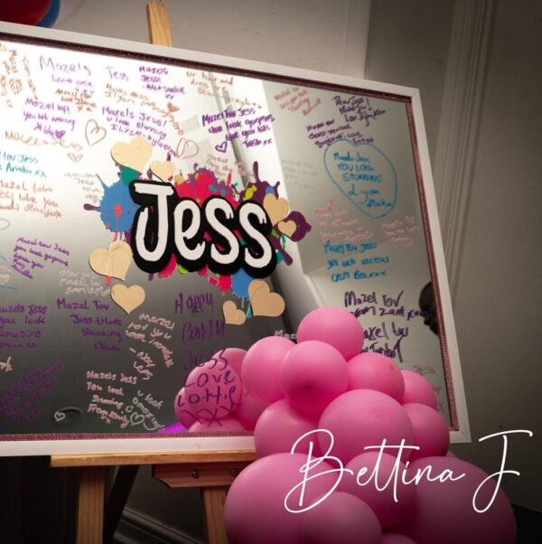 Decorative bespoke mirror with 'Jess' and colourful designs, surrounded by pink balloons.