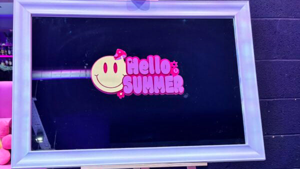 Bespoke mirror with 'Hello Summer' design on a stand against a dark wall.