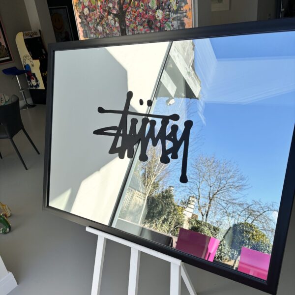 Bespoke mirror with a black logo on a stand in a room with colourful artwork in the background