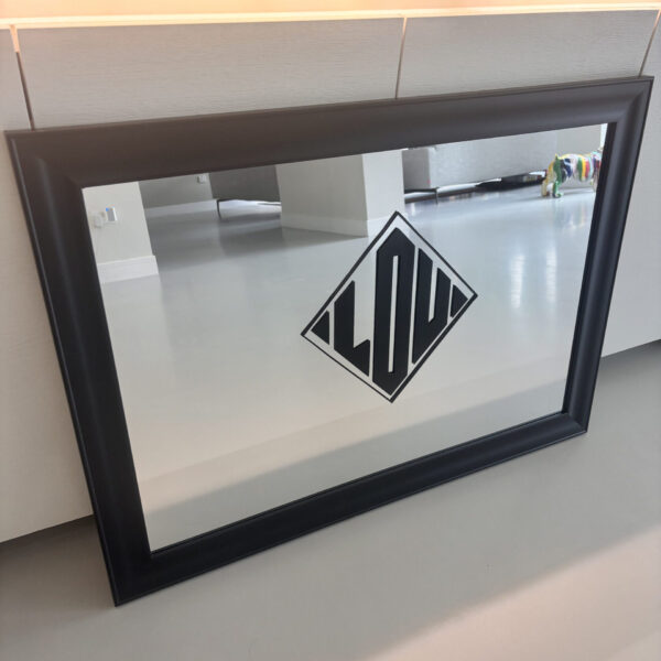 Black-framed bespoke mirror with a geometric design on a light-coloured wall.