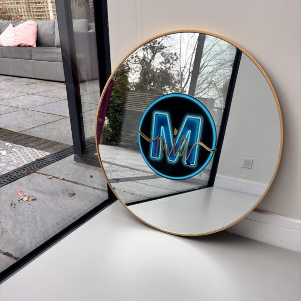 Round bespoke mirror with a gold frame on a white floor, reflecting a patio area.