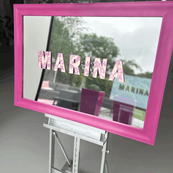 Pink-framed bespoke mirror with the name 'MARINA' on a stand outdoors.