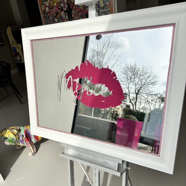 White-framed bespoke mirror with pink lips and 'Myles' logo on a white easel.