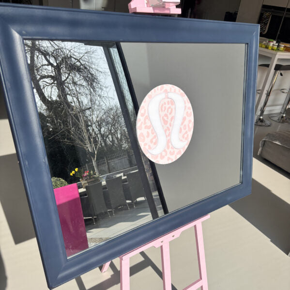 Blue-framed bespoke mirror on a pink stand with a blurred outdoor background
