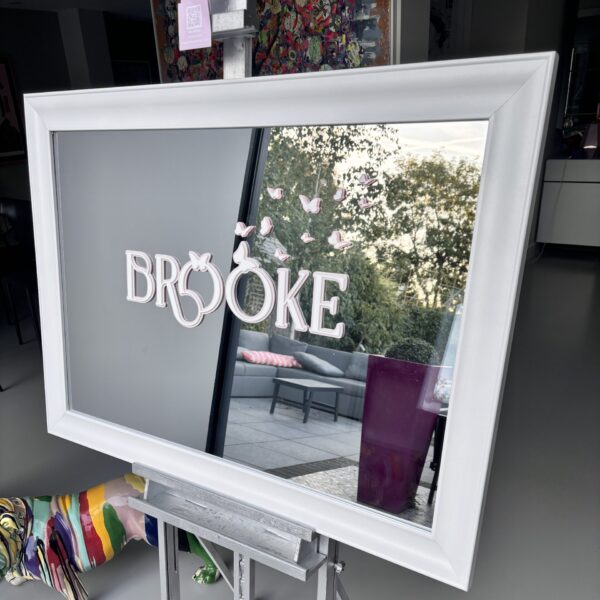 White-framed bespoke mirror with 'Brooke' branding, displaying an outdoor scene.