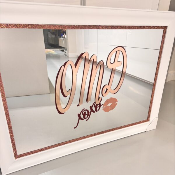 Decorative bespoke mirror with rose gold frame and text on a white surface