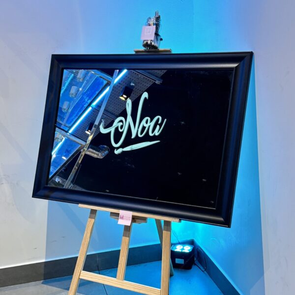 Black-framed bespoke mirror on an easel with 'Noa' in cursive, against a blue wall.