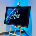 Black-framed bespoke mirror on an easel with 'Noa' in cursive, against a blue wall.