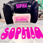 Black duffel bag and pink make up bag with 'Sophia' printed on them, placed on a white personalised pillow with 'Sophia' text.