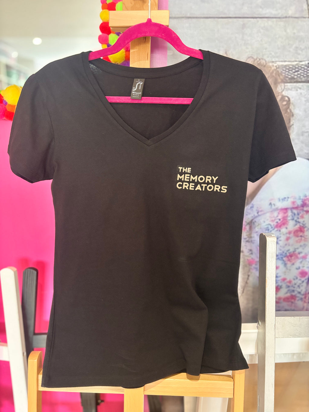 Black event t-shirt with 'The Memory Creators' text on a pink hanger against a colourful background.