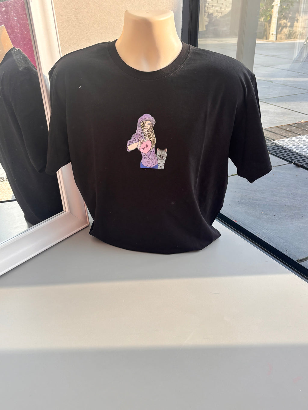 Black event t-shirt with a colourful graphic on a mannequin against a window background