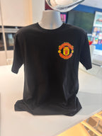 Black event t-shirt with a red and yellow Manchester United football club emblem on a mannequin in a store setting.