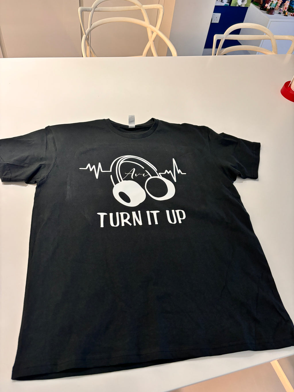 Black event t-shirt with white graphic design and text 'TURN IT UP' on a white surface.