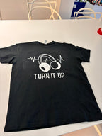 Black event t-shirt with white graphic design and text 'TURN IT UP' on a white surface.