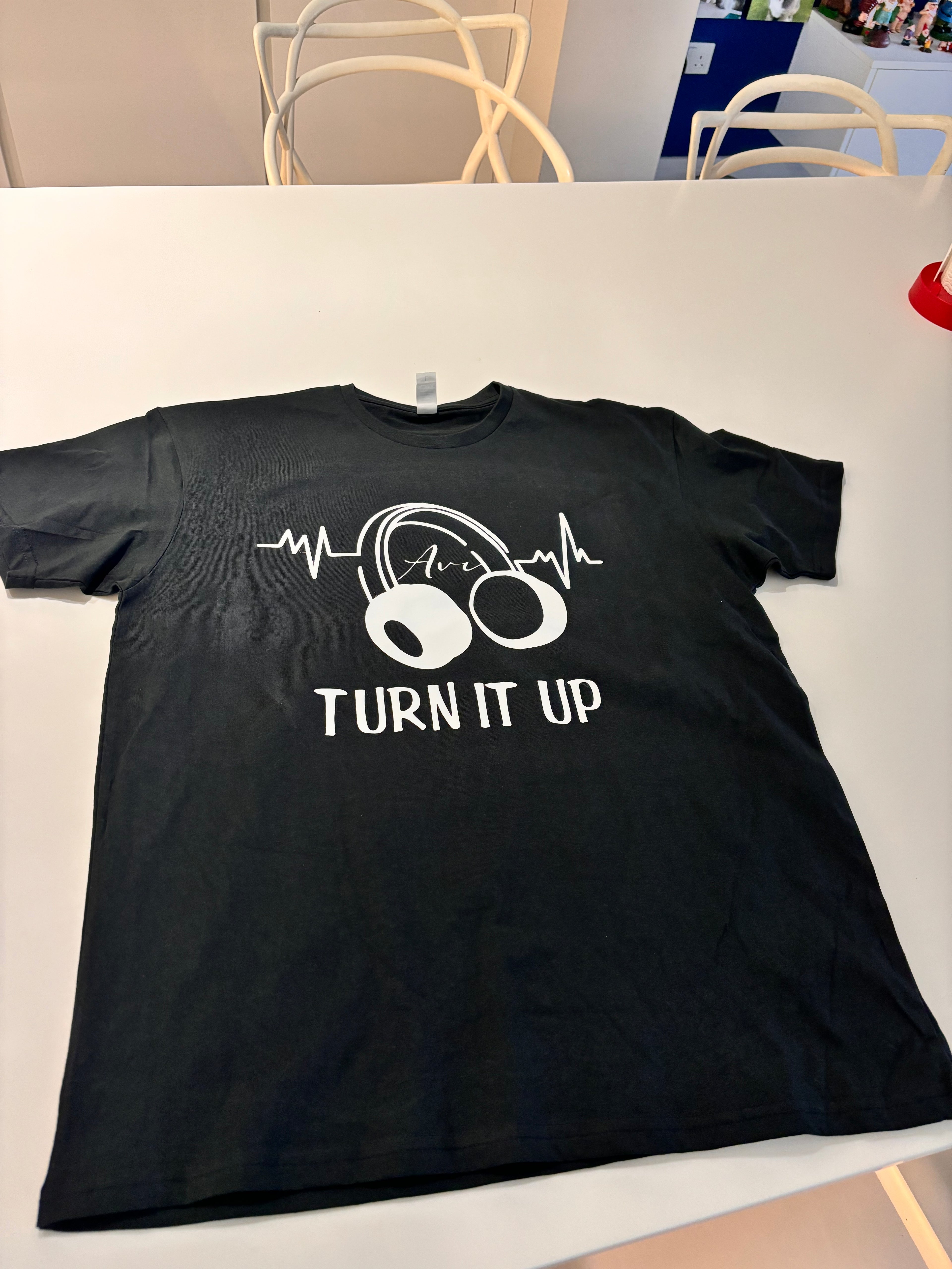 Black event t-shirt with white graphic design and text 'TURN IT UP' on a white surface.