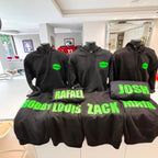 Black hoodies with green names on mannequins in a room.
