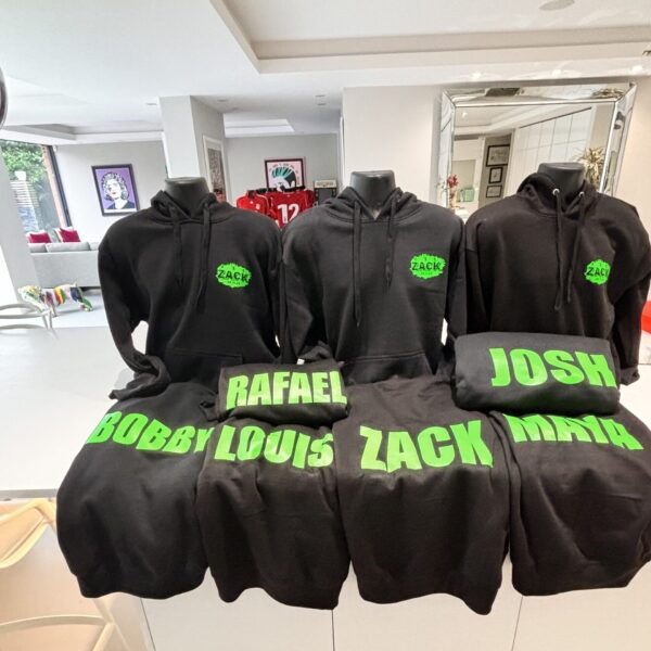 Black hoodies with green names on mannequins in a room.