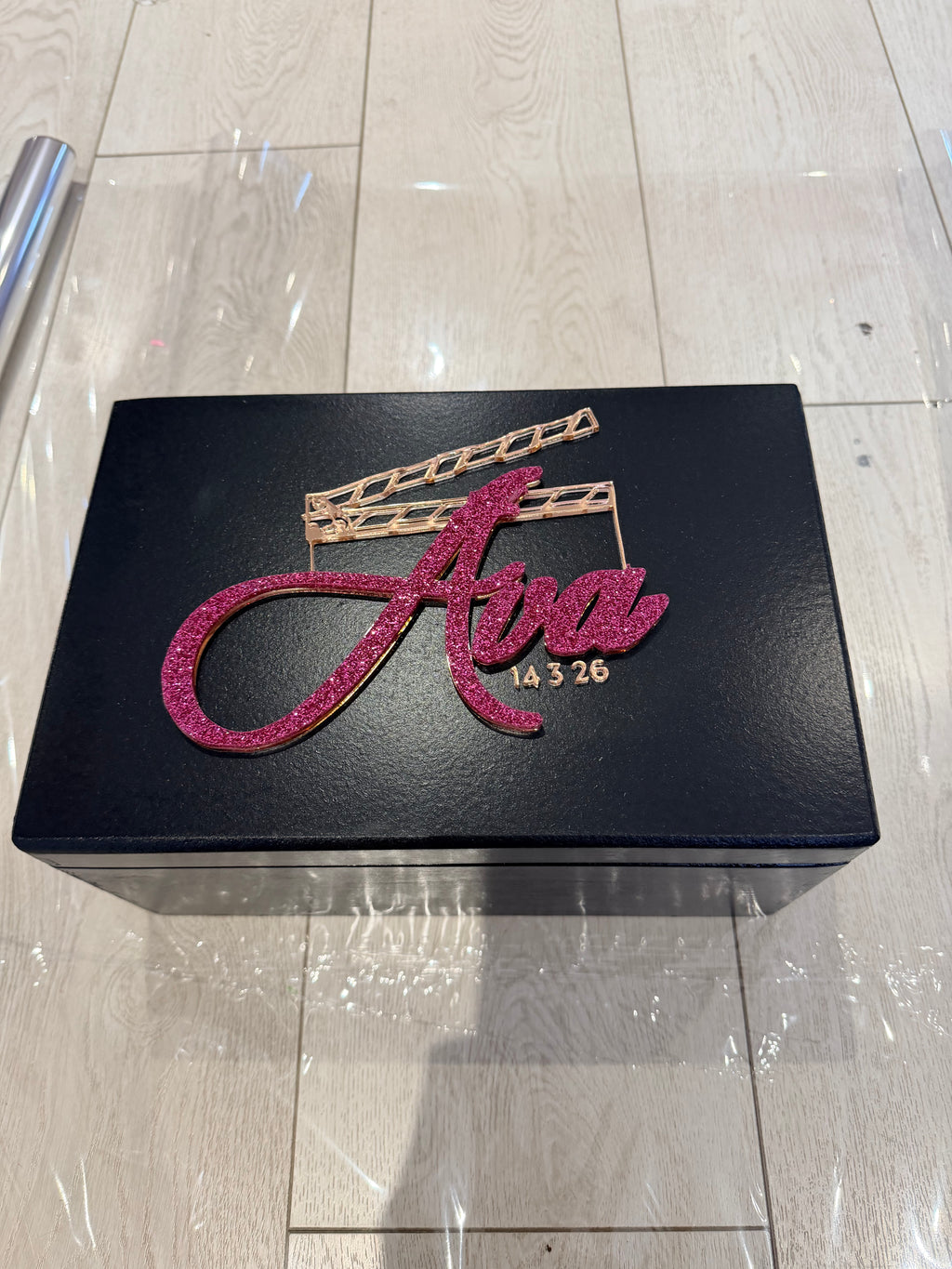 Black keepsake box with pink and gold movie design on a tiled floor