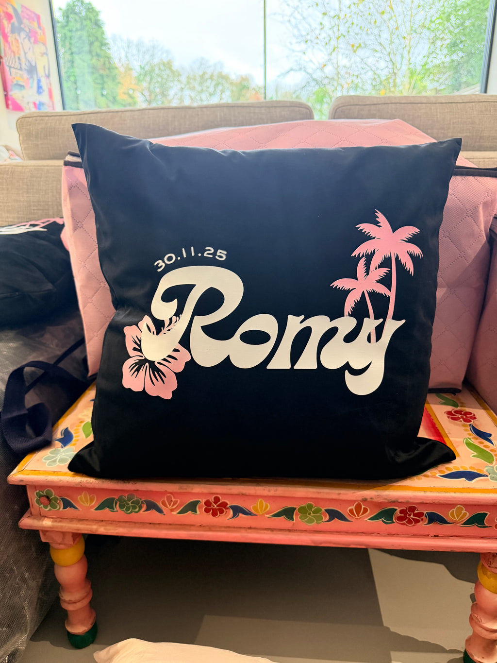 Black logo pillow with 'Romantic' text and palm tree designs on a colourful chair.