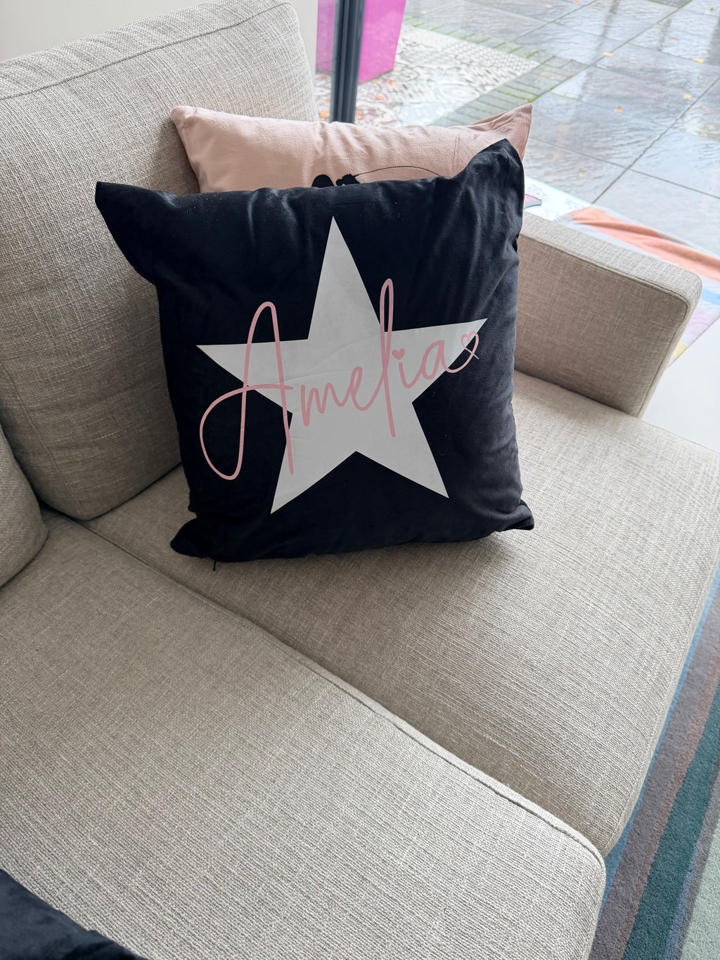 Black logo pillow with a white star and 'Amelie' text on a grey couch.