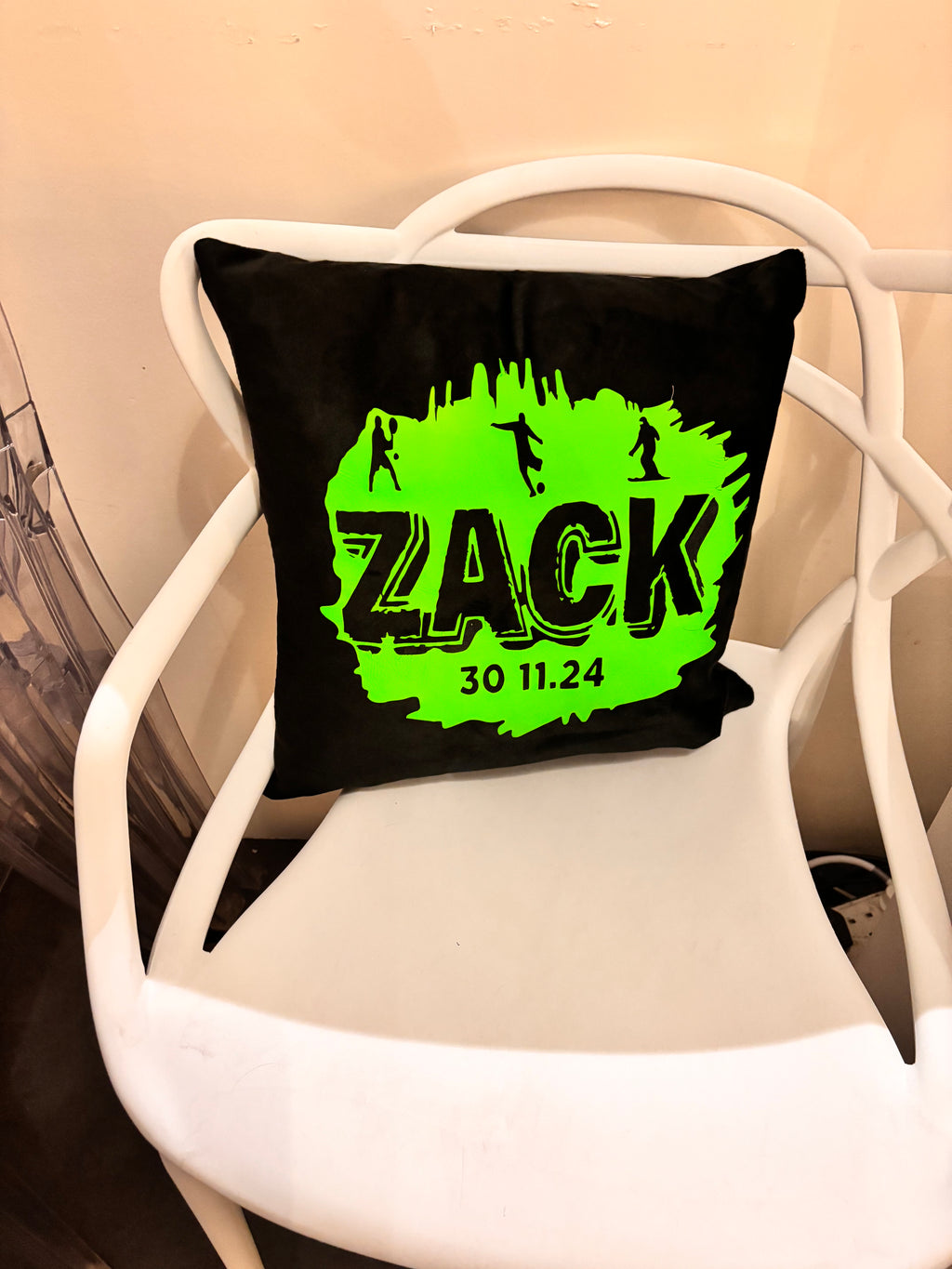 Black logo pillow with green text 'ZACK' on a white chair.