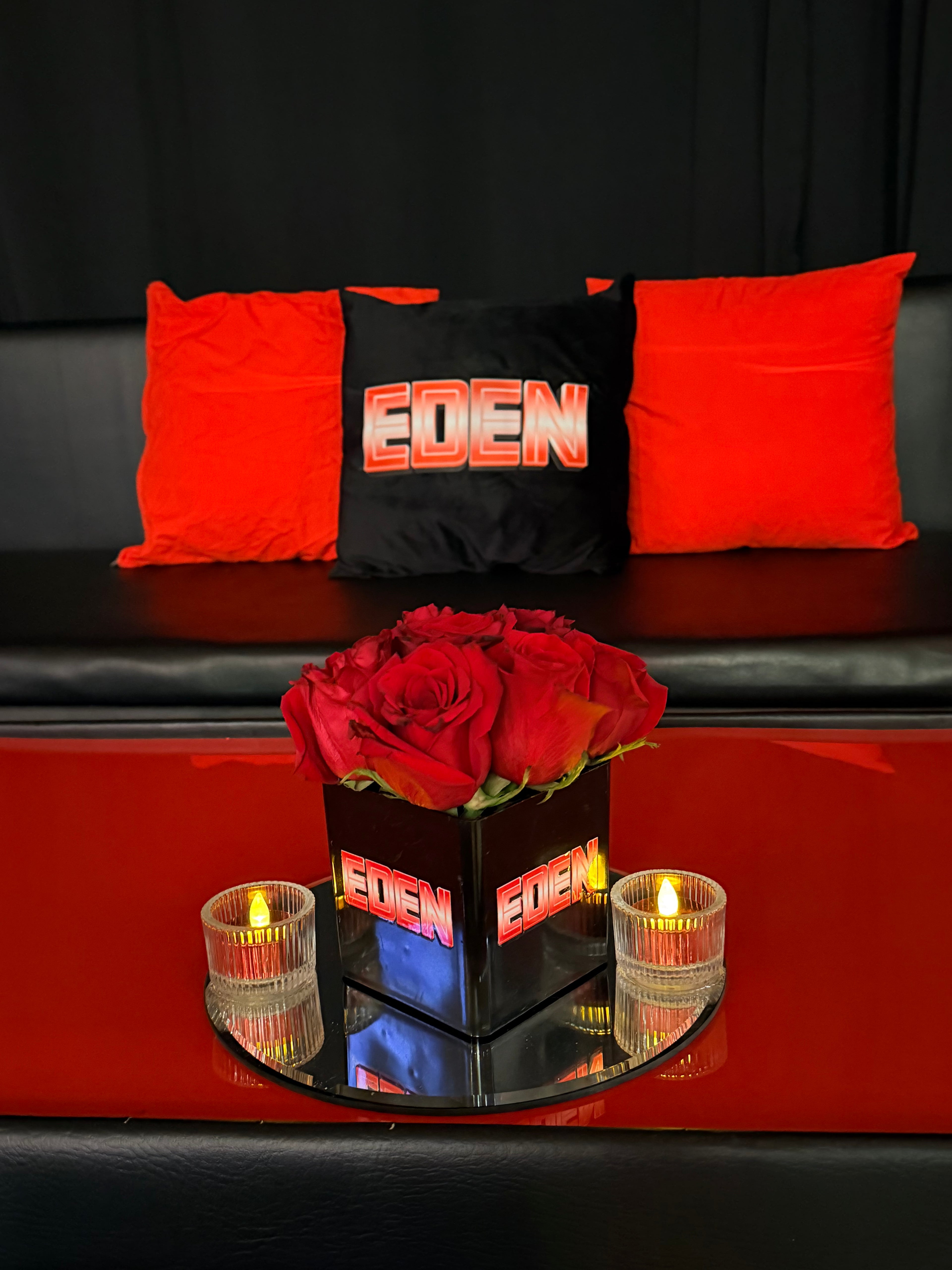 Black logo pillow with red text on a bed next to red roses.