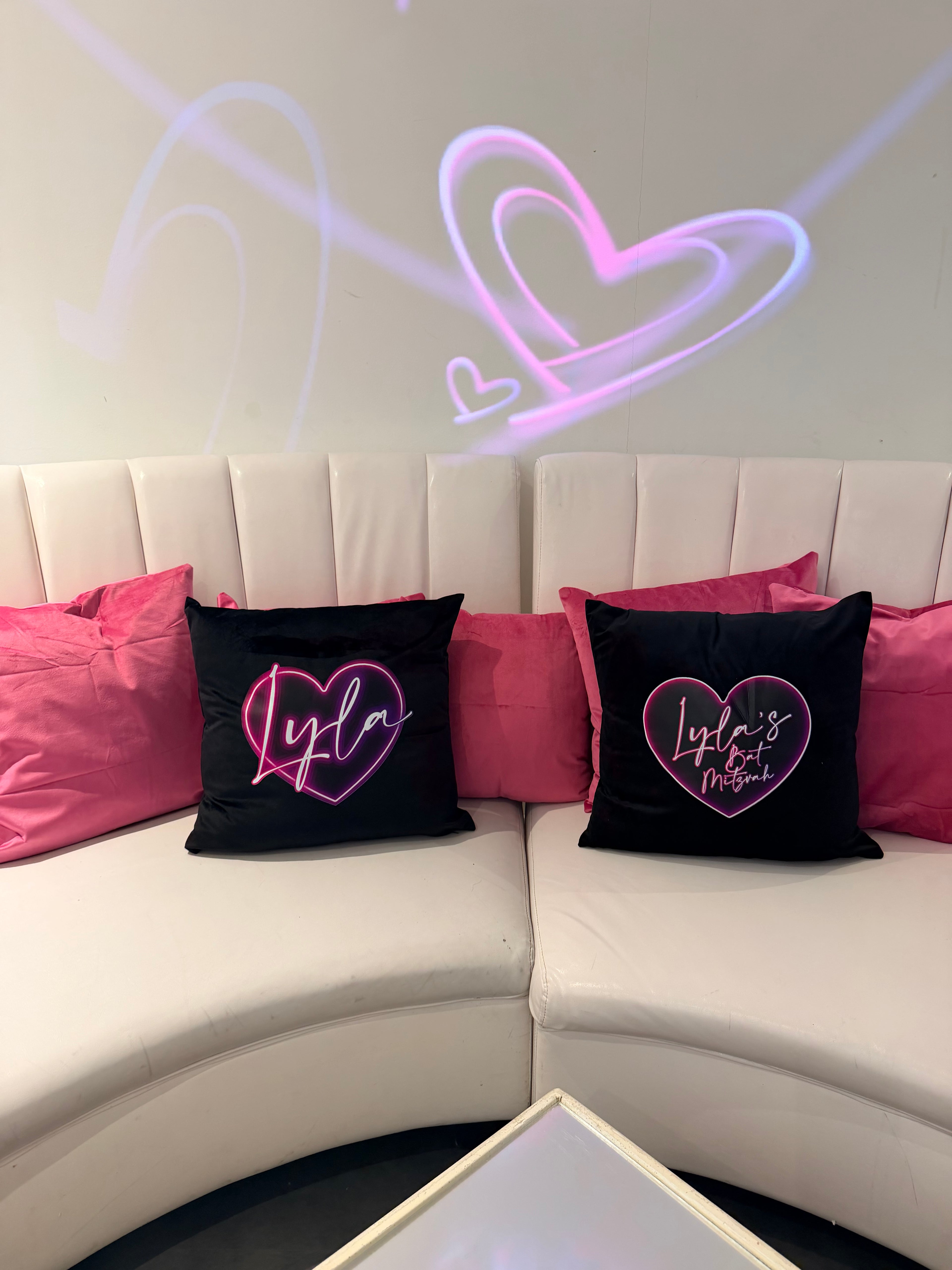 Black logo pillows with pink heart designs amongst pink pillows