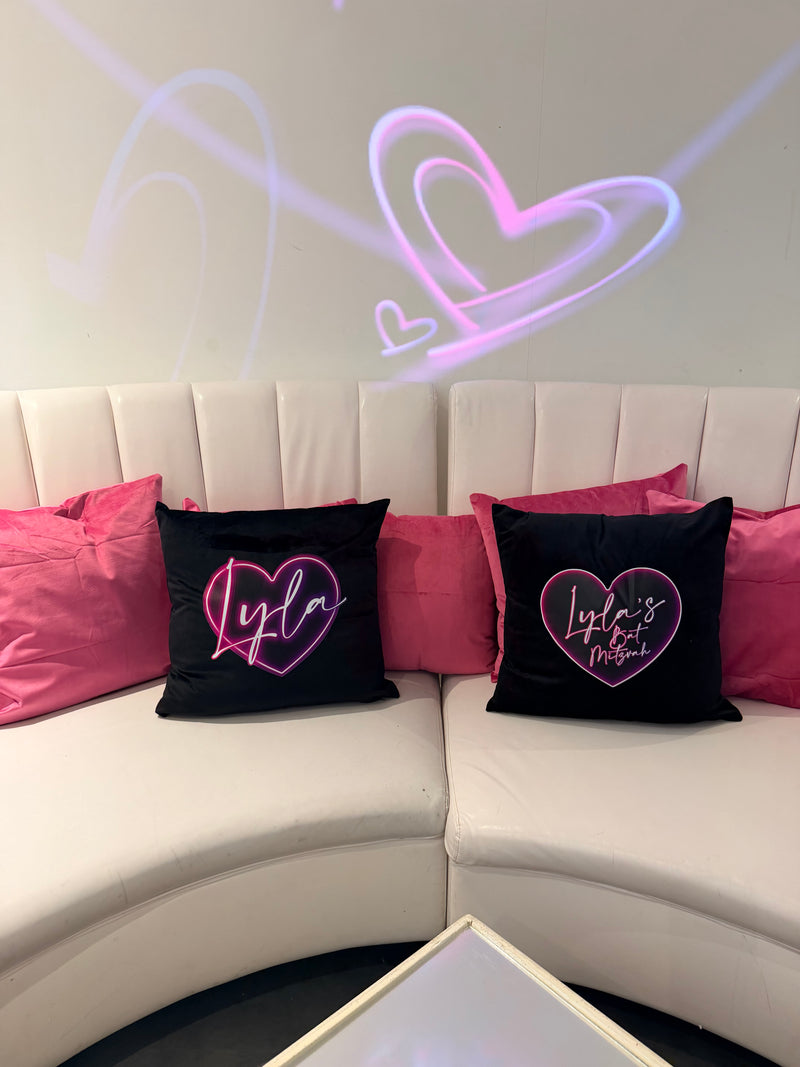 Black logo pillows with pink heart designs amongst pink pillows