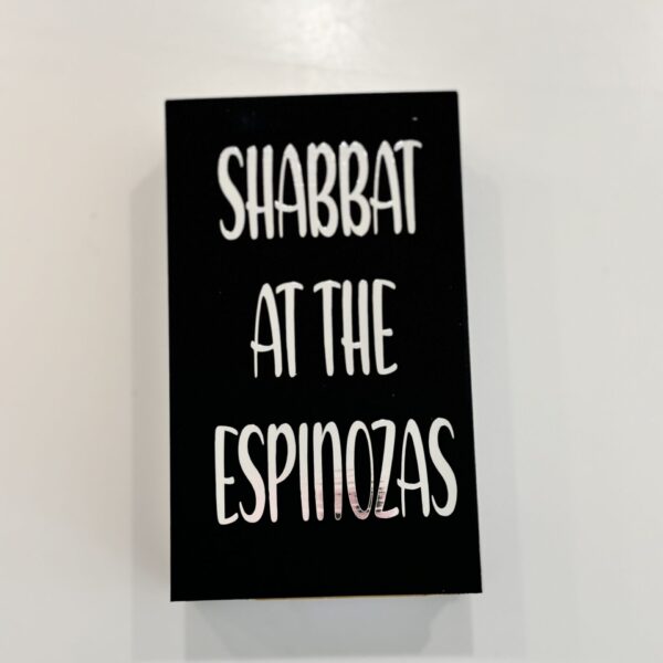 Black match box sleeve with white text 'SHABBAT AT THE ESPINOZAS' on a light grey background