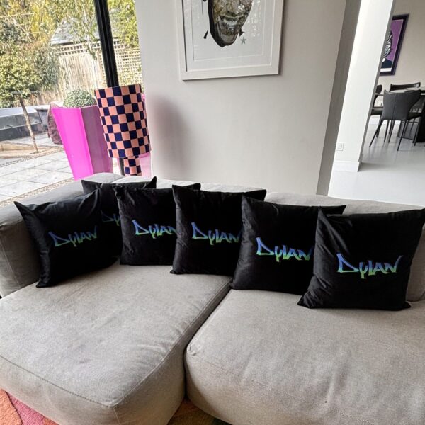 Black personalised silk pillow cases with 'Dylan' branding on a grey sofa in a living room.