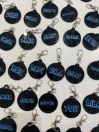 Black round keyrings with blue personalised name text on a white background