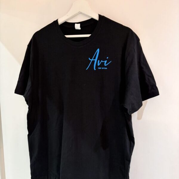 Black t-shirt with 'Avi' logo on a hanger against a beige wall