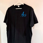 Black t-shirt with 'Avi' logo on a hanger against a beige wall