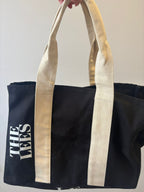 Black tote bag with beige handles and 'THE LEES' branding on a light background