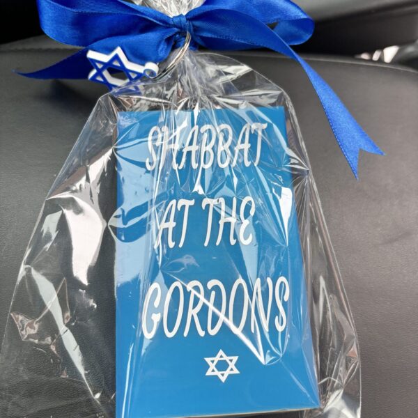 Blue match box sleeve with 'Shabbat at the Gordons' text and Star of David, wrapped in clear cellophane with a blue ribbon.