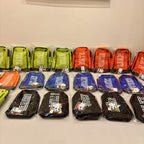 Row of colourful boot bags with visible branding on a white surface.