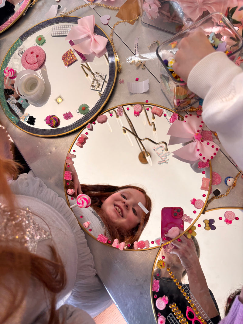 Child looking into a decorative mirror with floral and decorative elements taken at a Mirrored Memories mirror party
