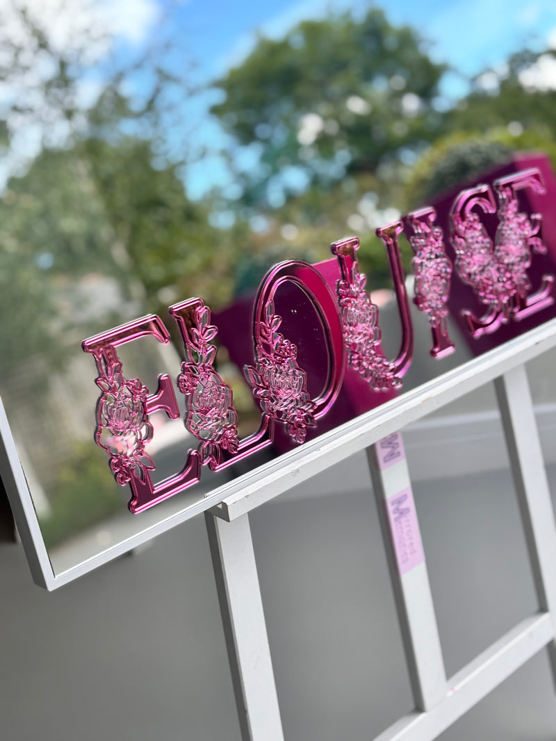 Classic mirror in a white frame with a pink decorative sign with 'LOVE' in acrylic on a white stand outdoors