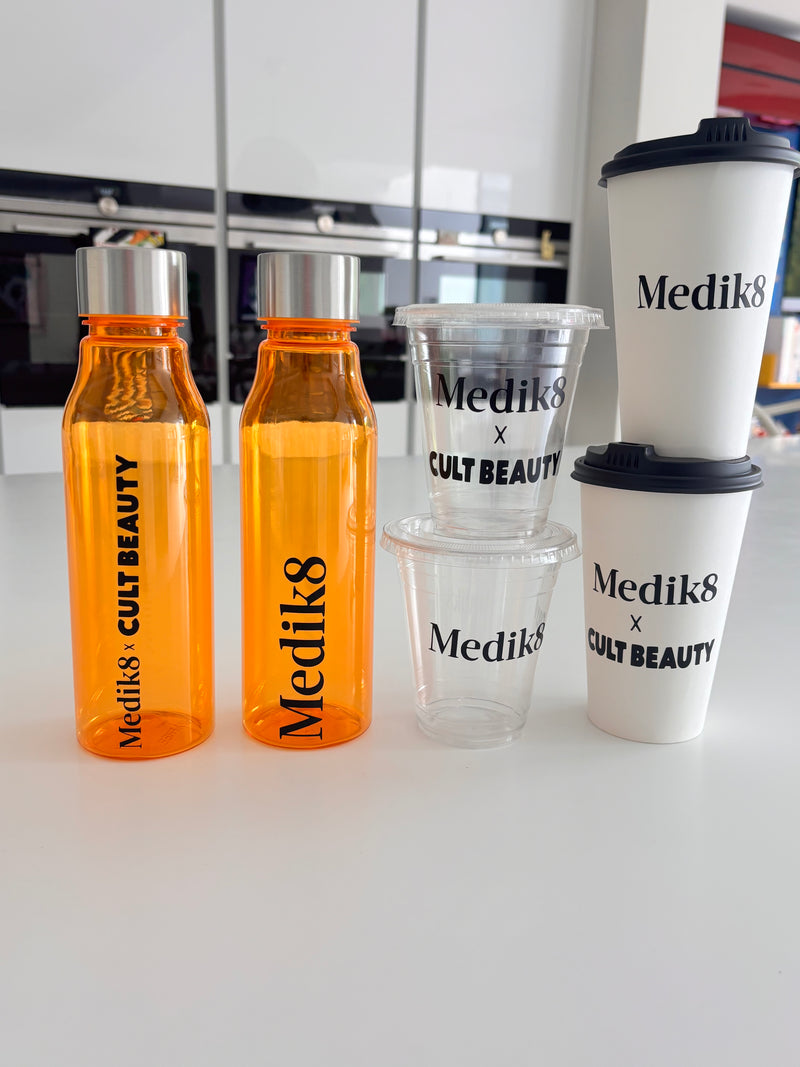 Collection of corporate gifting for Medik8 clear cups, hot cups and orange flasks on a white surface