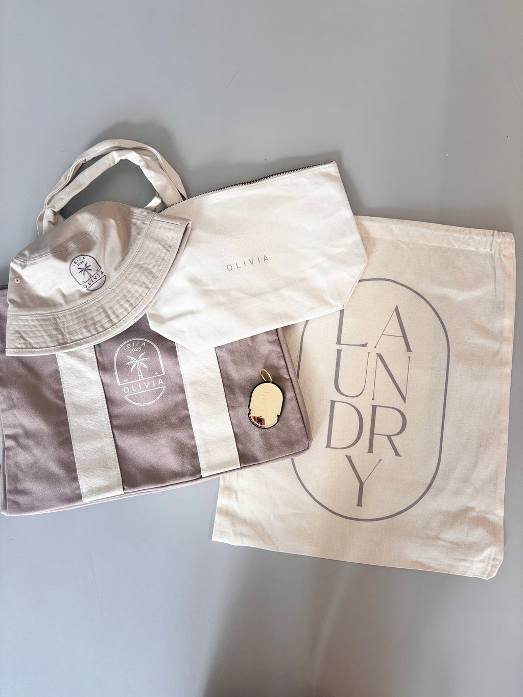 Collection of personalised bags including a hat, tote bag, and laundry bag on a grey background