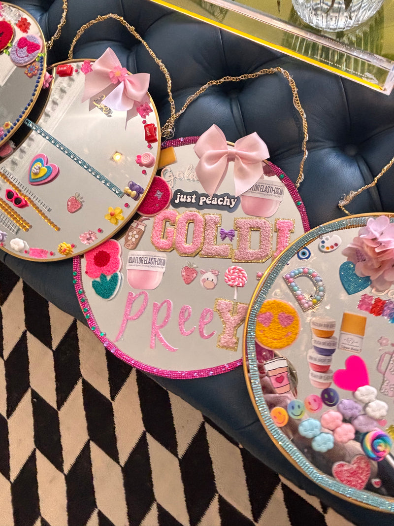 Decorative heart-shaped mirrors with colourful designs and text on a black leather surface from a Mirrored Memories mirror party