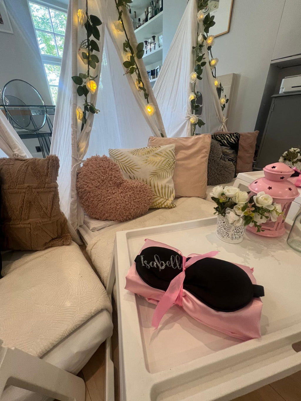 Decorative personalised pillow setup with pillows, a coffee table, sleep mask and fairy lights in a room.