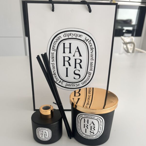 Two black candles with wooden lids and Diptyque-style branding in front of a Diptyque-style branded box.