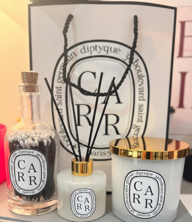 Diptyque style dffuser, candle, and match bottle with decorative sticks against a Diptyque-style  branded background.